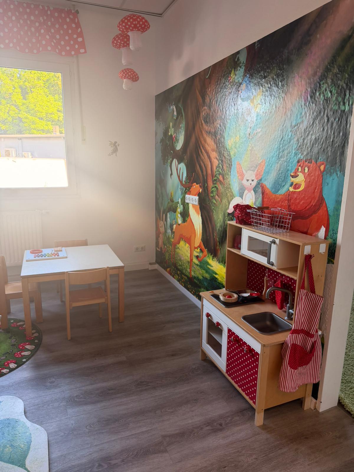 Kinderküche und kleiner Tisch vor einer Waldmalerei